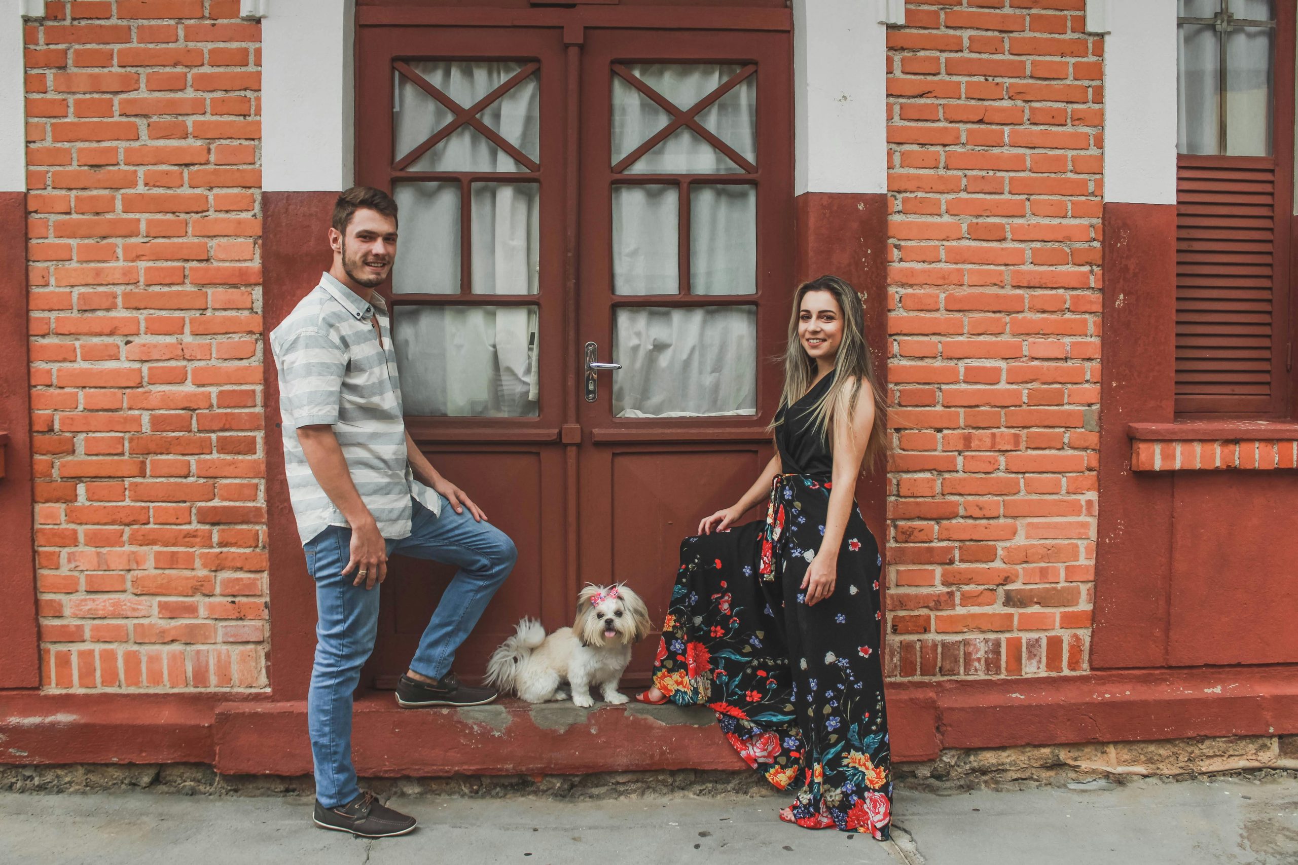 Smiling couple poses with fluffy dog in front of a classic brick house doorway.