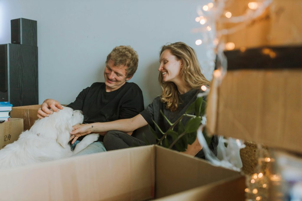 A cheerful couple bonding with their dog amid moving boxes, embracing a fresh start.