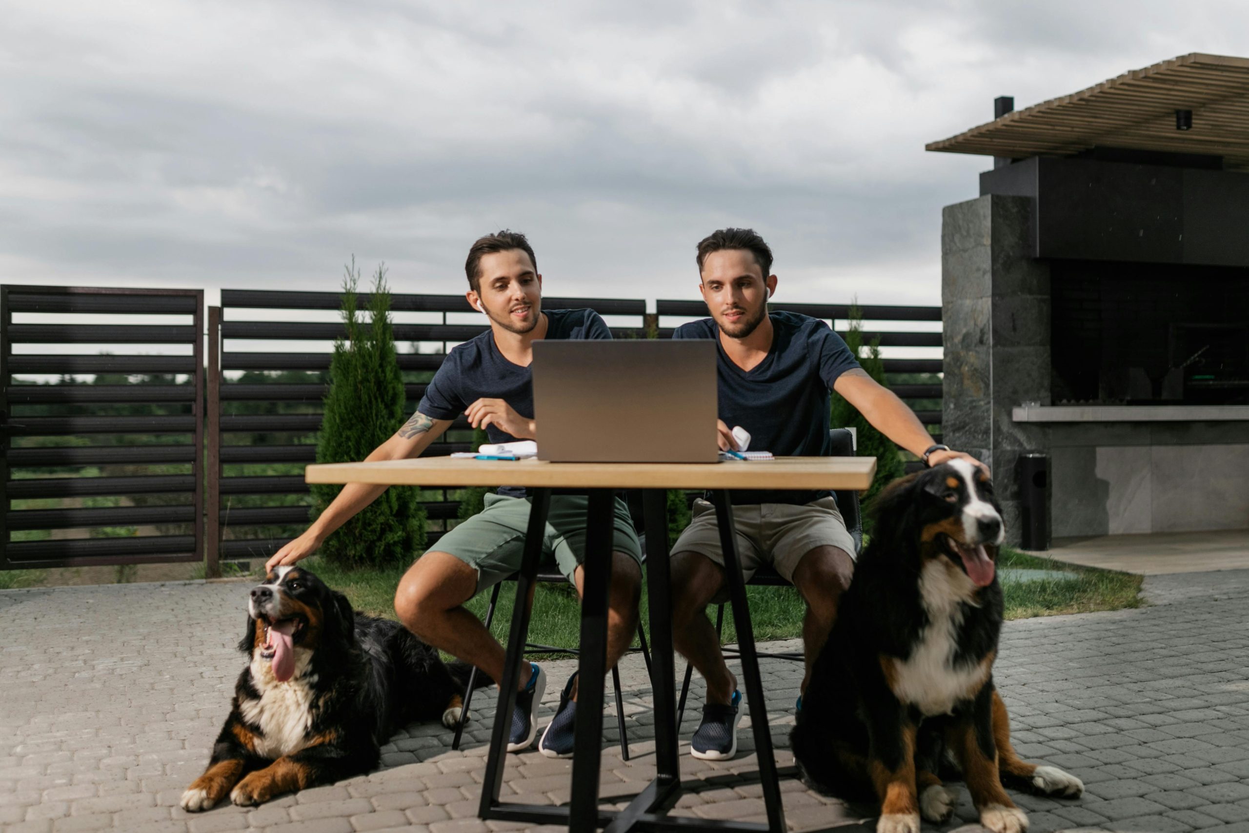 Twins working on a laptop outside with their Bernese Mountain Dogs.